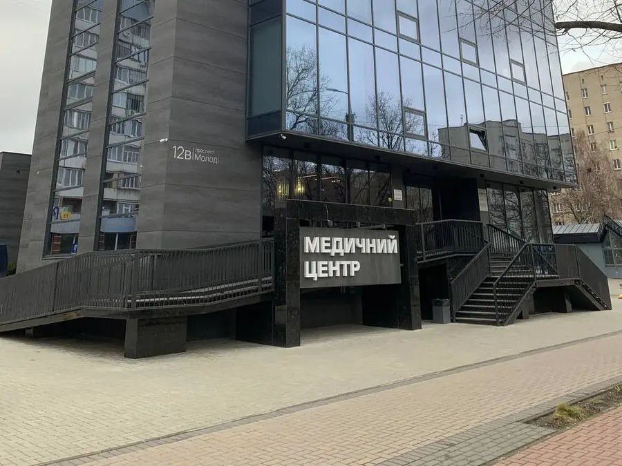 Будівля медичного центру «Медикал Плюс» на розі проспекту Молоді: скляний фасад, вивіска «Медичний центр», табличка з номером 12В